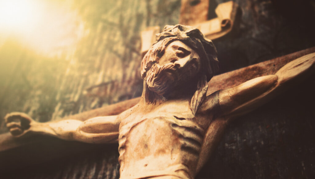 Antique wooden statue of crucified Jesus Christ against dark wooden background